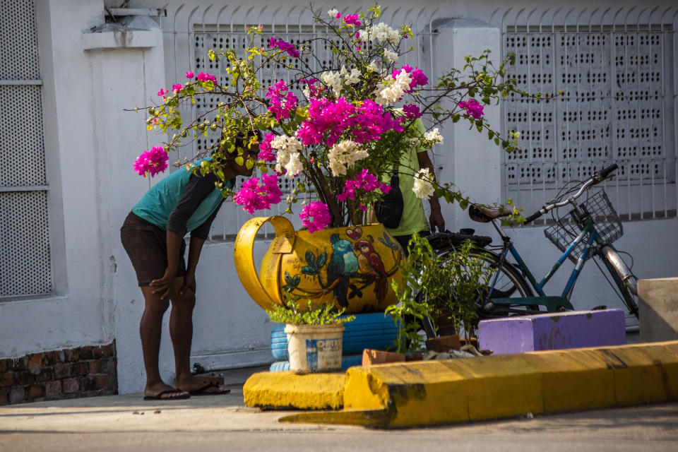People stand behind a sidewalk flower pot watch as soldiers and police remove improvised barricades installed by anti-coup protesters and residents to secure a neighborhood from security forces in Yangon, Myanmar Thursday, March 18, 2021. (AP Photo)