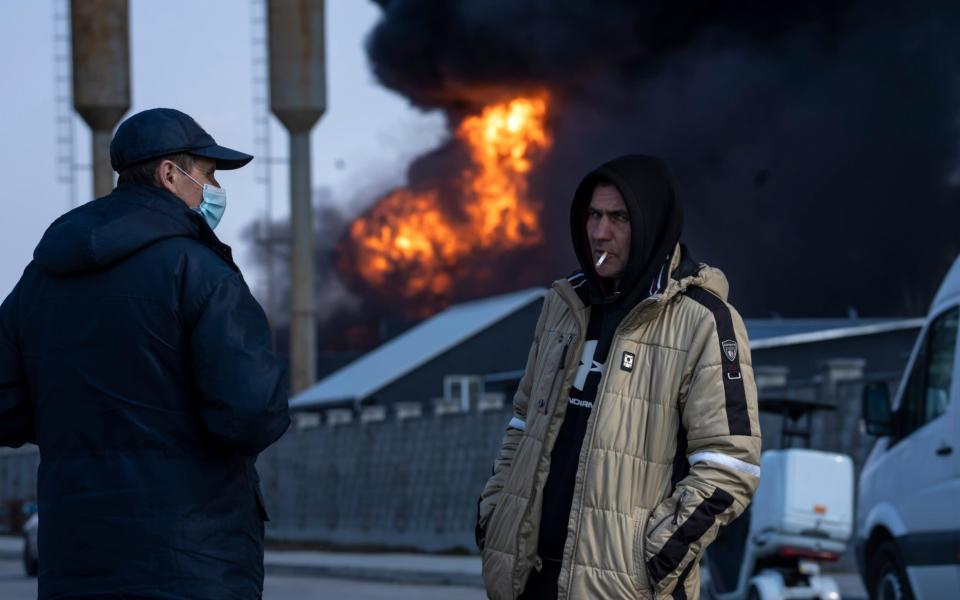 Men stand near flames from fuel storage of the Ukrainian army following a Russian attack, on the outskirts of Kyiv, Ukraine - Rodrigo Abd/AP
