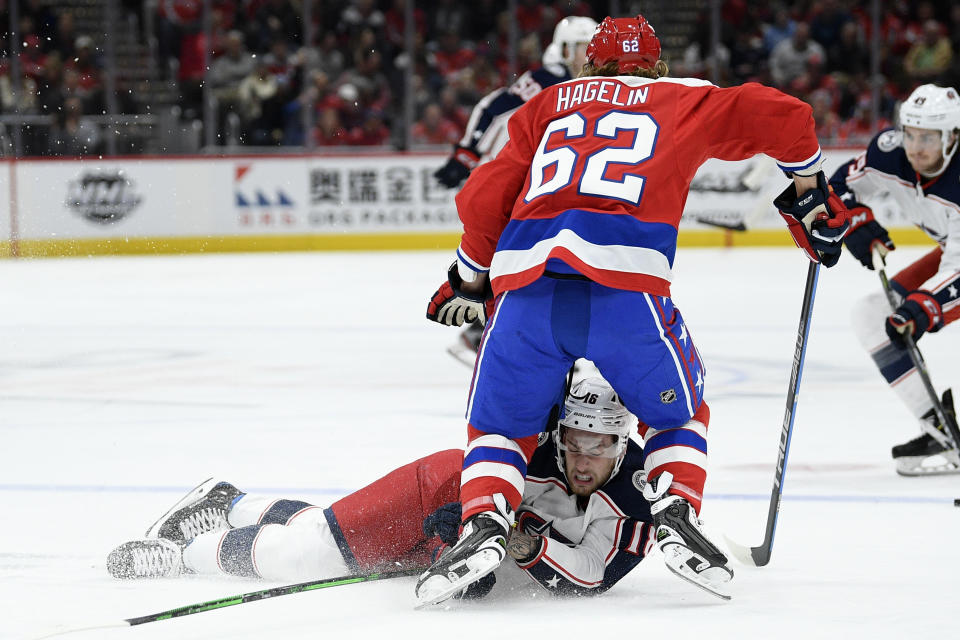 Columbus Blue Jackets center Pierre-Luc Dubois (18) lies on the ice below Washington Capitals left wing Carl Hagelin (62) during the first period of an NHL hockey game Friday, Dec. 27, 2019, in Washington. (AP Photo/Nick Wass)
