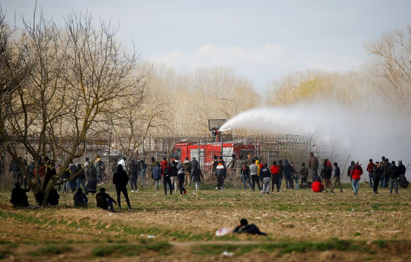 A Greek fire fighter uses a water cannon as migrants look on near Turkey's Pazarkule border crossing with Greece's Kastanies, near Edirne