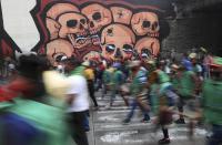 Indigenous protesters walk past a mural of skulls as they march against the government in Bogota, Colombia, Monday, Oct. 19, 2020. The leaders of the indigenous communities say they are mobilizing to reject massacres, assassinations of social leaders, criminalization of social protest, to defend their territory, democracy and peace, and plan to stay in the capital for a nationwide protest and strike on Oct. 21. (AP Photo/Fernando Vergara)