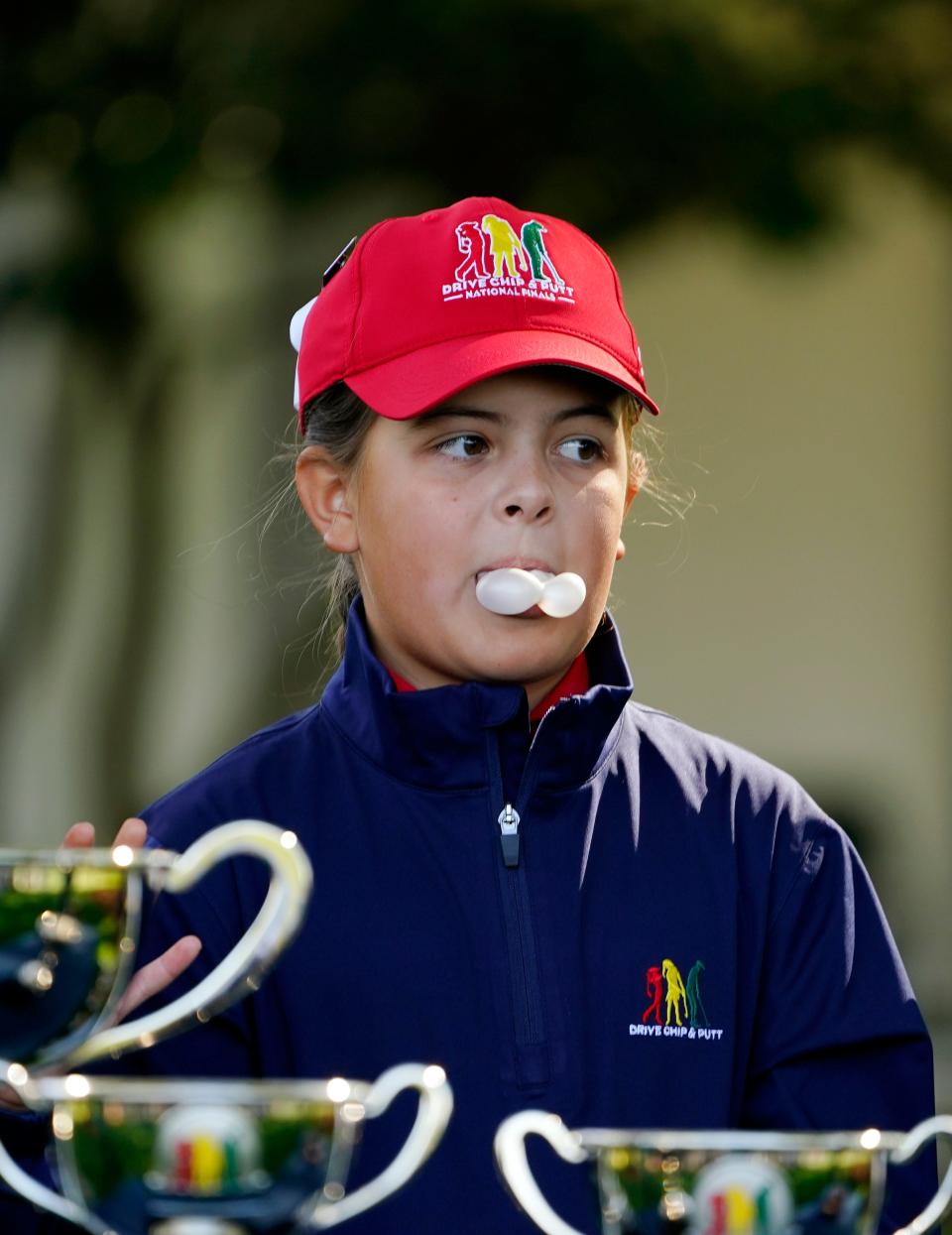 Madleyn Dickeerson blows a bubble during the awards presentations at the Drive, Chip & Putt National Finals competition at Augusta National Golf Club.