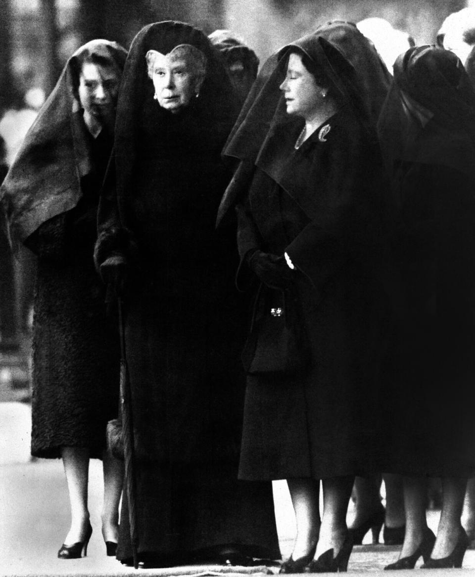 Three women wearing dark clothing and veils stand waiting