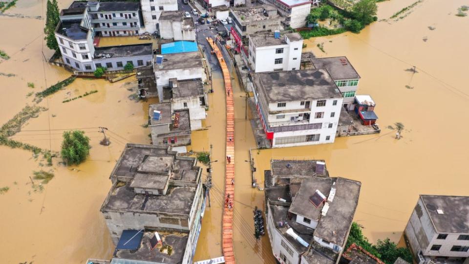 an aerial photograph shows a street of buildings all submerged in water and a central walkway build above the floodwaters in the center, people are walking along it.