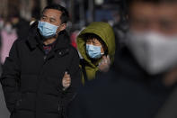 A woman wearing a face mask and gloves to protect from the coronavirus walks with her masked partner at the Wangfujing shopping district in Beijing on Dec. 12, 2021. China’s attitude toward the virus, omicron or not, is to stop transmission in its tracks, and the country appears to be getting even tougher with the approach of the Beijing Winter Olympics in February. (AP Photo/Andy Wong)