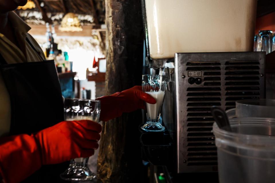 A person holds a glass with white liquid under a beverage dispenser