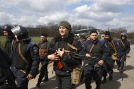 Ukrainian police walk along a road as Ukrainian army troops receive ammunition in a field on the outskirts of Izyum, Eastern Ukraine, Tuesday, April 15, 2014. An Associated Press reporter saw at least 14 armored personnel carriers with Ukrainian flags, one helicopter and military trucks parked 40 kilometers (24 miles) north of the city on Tuesday. (AP Photo/Sergei Grits)