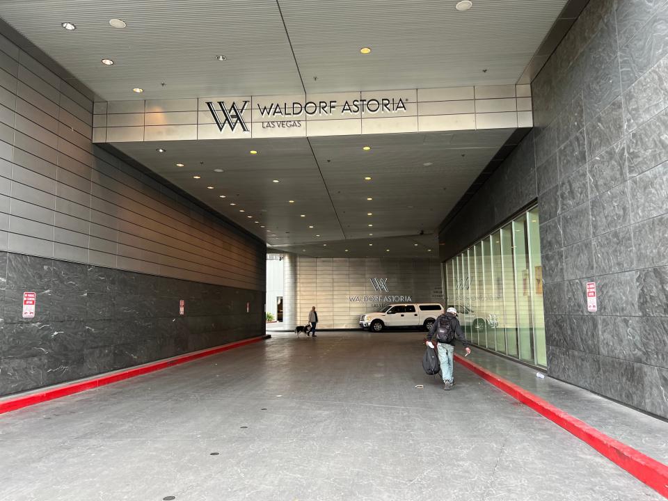 A driveway leading into the entrance to the Waldorf Astoria Las Vegas with a man walking and a parked car.