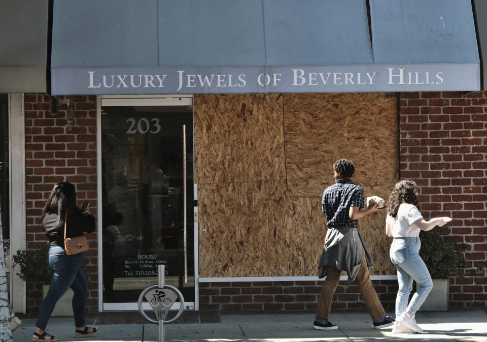 Pedestrians walk past a boarded up Luxury Jewels of Beverly Hills on Wednesday, March 23, 2022 in Beverly Hills, Calif. Los Angeles police are warning people that wearing expensive jewelry in public could make them a target for thieves — a note of caution as robberies are up citywide. The police department's suggestion Tuesday, March 22, came as robbers smashed the front window of a Beverly Hills jewelry store in broad daylight and fled with millions of dollars' worth of merchandise. (AP Photo/Richard Vogel)
