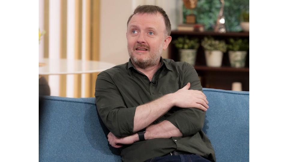 Chris McCausland on blue sofa in khaki shirt