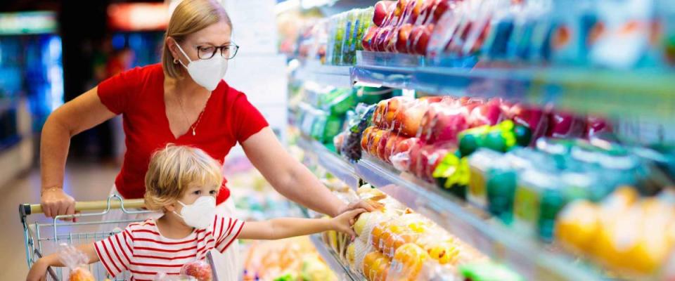 Shopping with kids during virus outbreak. Mother and child wearing surgical face mask buying fruit in supermarket. Mom and little boy buy fresh vegetable in grocery store. Family in shop.