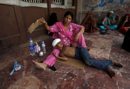 A woman uses a piece of cardboard to fan her son, while waiting for their turn for a medical checkup, outside Jinnah Postgraduate Medical Centre (JPMC) during intense hot weather in Karachi, Pakistan, June 23, 2015. REUTERS/Akhtar Soomro