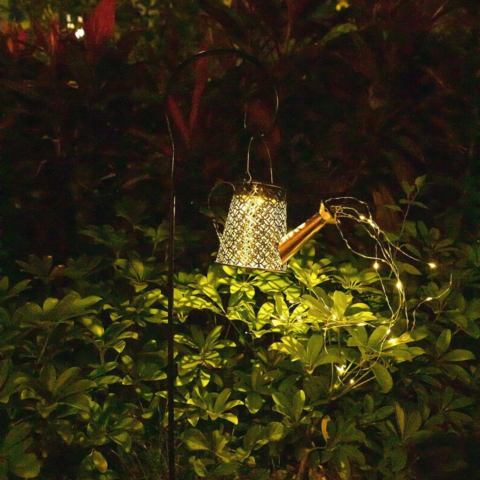 Outdoor hook light shaped like a watering can with string lights coming out of spout