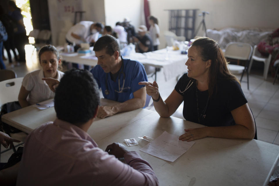 In this Oct. 26, 2019, photo, Dr. Julie Sierra, of San Diego, right, talks with a migrant couple during a clinic at a shelter in Tijuana, Mexico. A burgeoning grassroots movement of health professionals and medical students from both sides of the U.S.-Mexico border is quietly battling on the front lines to keep asylum seekers healthy and safe. It is a daunting task taken on by volunteers trying to desperately tend to a need left largely unmet by the governments of both countries. (AP Photo/Gregory Bull)