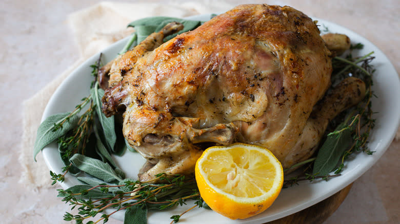 whole chicken on platter with herbs, lemon