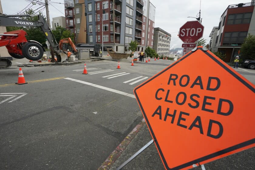 A sign is shown near ongoing work on a project to replace water main pipes, Wednesday, June 15, 2022, in downtown Tacoma, Wash. Inflation is taking a toll on infrastructure projects across the U.S., driving up costs so much that state and local officials are postponing projects, scaling back others and reprioritizing their needs. (AP Photo/Ted S. Warren)