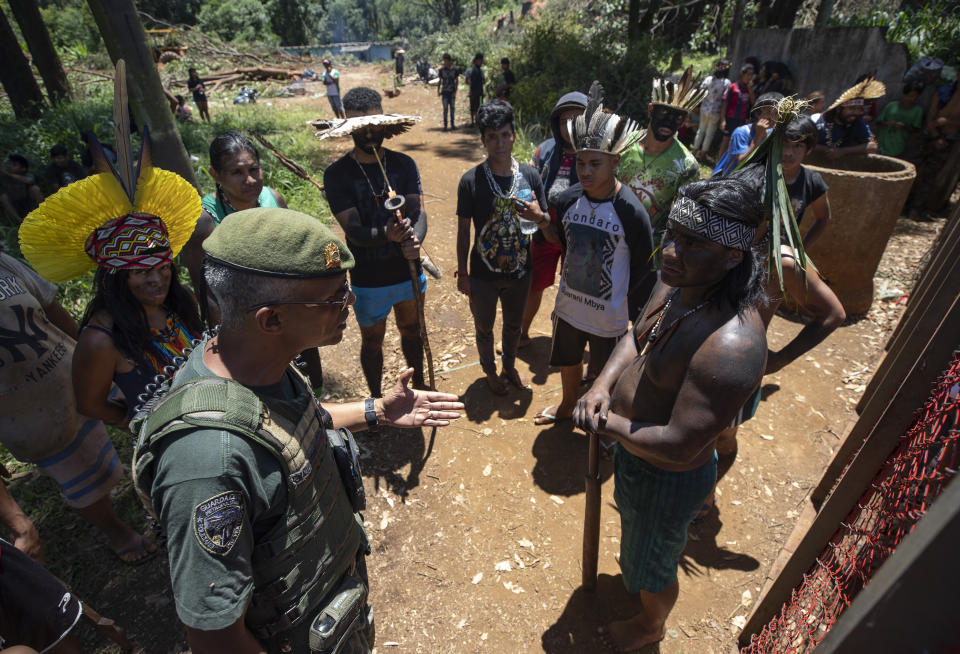 A police officer asks David Karai, a leader within the Guarani Mbya indigenous tribe, for his group to leave the property where real estate developer Tenda cut trees to make way for apartment buildings, next to the indigenous community's land in Sao Paulo, Brazil, Thursday, Jan. 30, 2020. The tension between a builder with projects in nine Brazilian states and a 40-family indigenous community is a microcosm of what’s playing out elsewhere in the country. (AP Photo/Andre Penner)