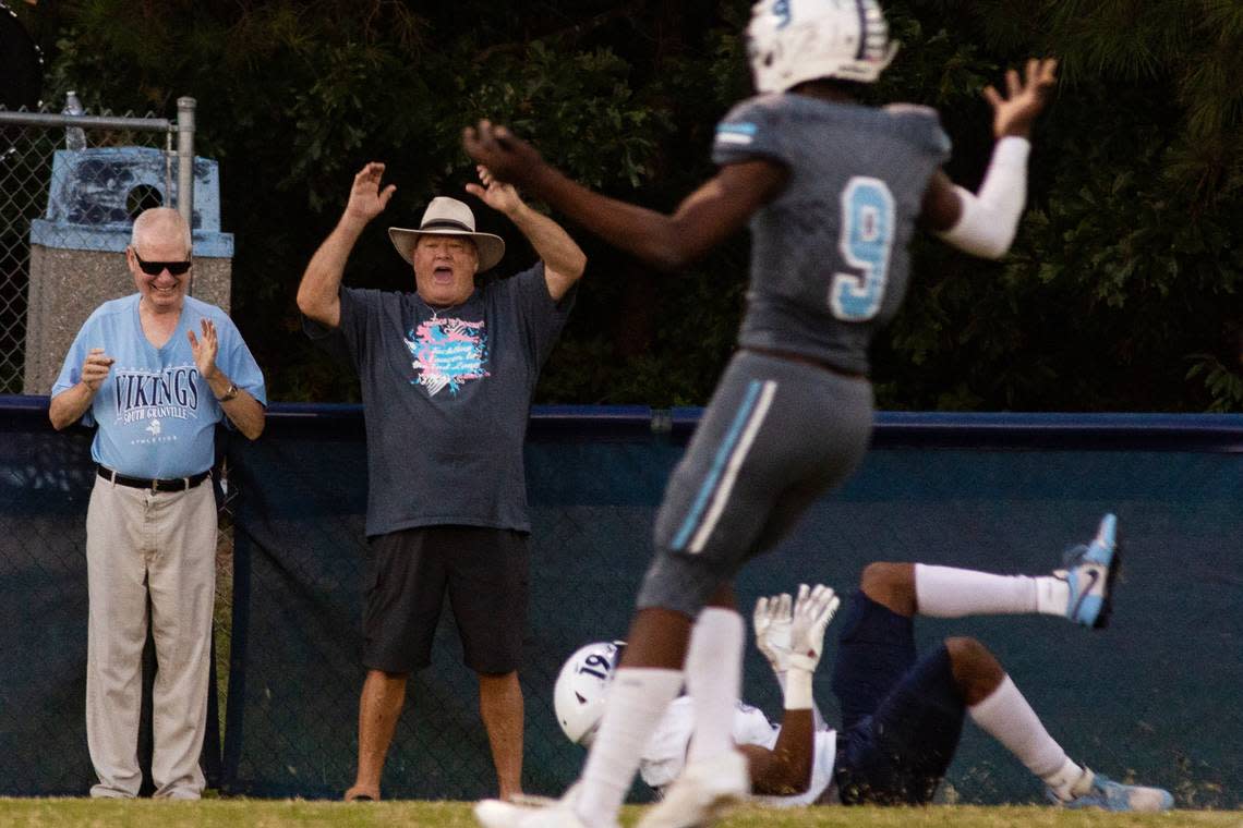 Tom Husketh (left) and Hayden Shackelford stand on the sidelines beyond the home bleachers during a game at South Granville High School. Husketh and Shackelford have permission from Michael Hobgood, South Granville’s football coach, to position themselves near the action. Husketh is blind, and Shackelford narrates the play-by-play to him.