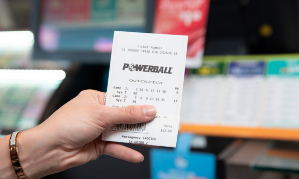 A woman holds a Powerball lottery ticket while standing in a newsagency.