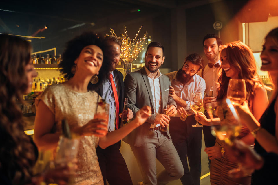 Group of friends laughing and toasting with drinks at a festive gathering