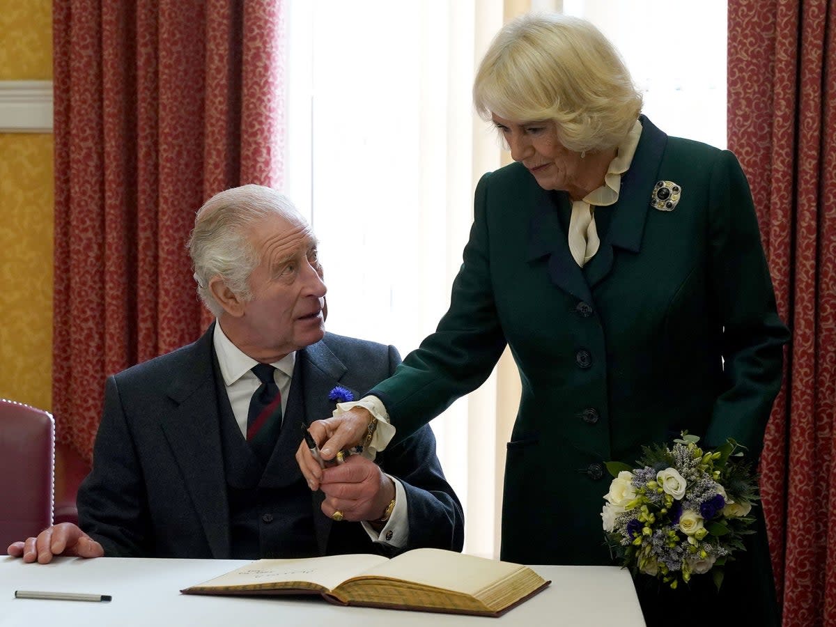 King Charles III (L) and Britain's Camilla, Queen Consort hold a pen as they sign a visitors' bok after attending an official council meeting at the City Chambers in Dunfermline (POOL/AFP via Getty Images)