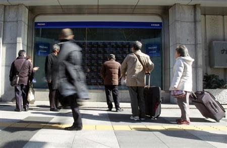 Pedestrians look at an electronic board showing stock prices outside a brokerage in Tokyo February 18, 2014. REUTERS/Yuya Shino