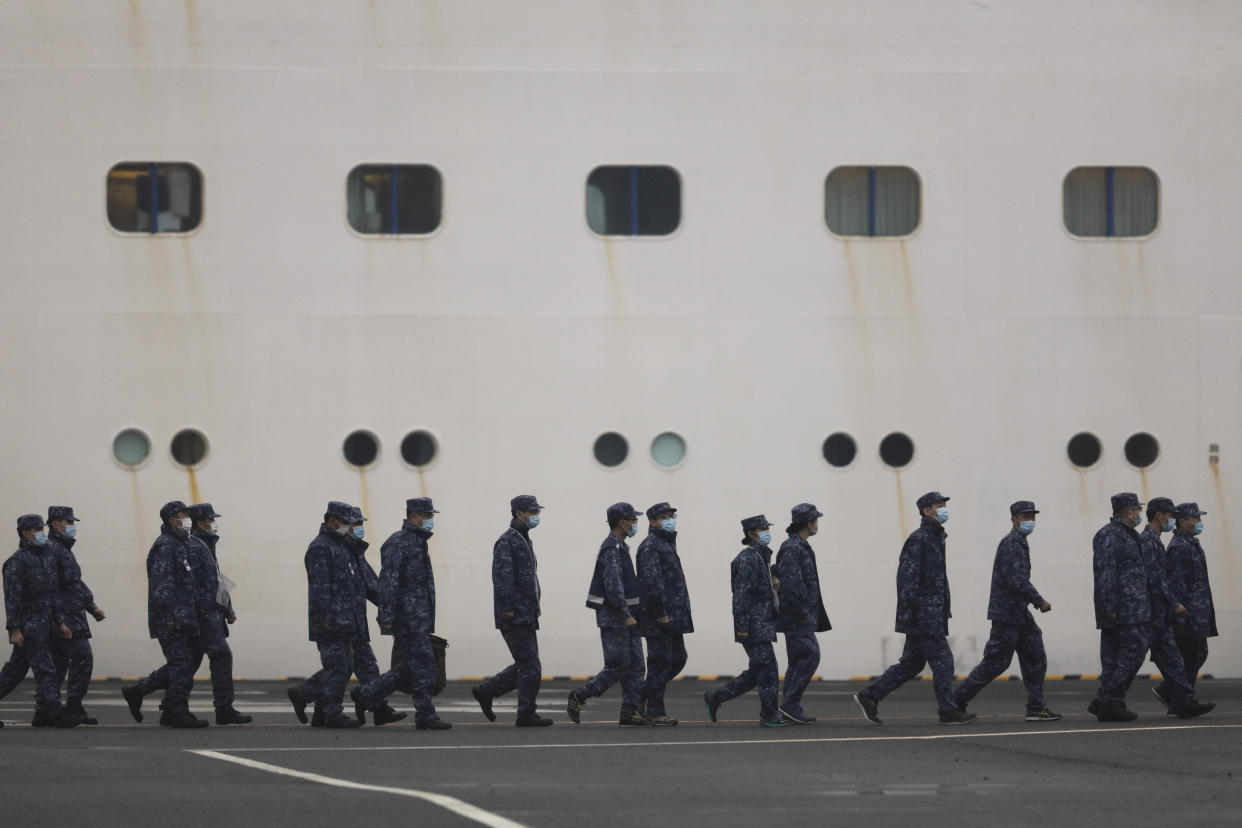 Members of Japan Self-Defense Forces walk past the quarantined Diamond Princess cruise ship Sunday, Feb. 16, 2020, in Yokohama, near Tokyo. The U.S. says Americans aboard a quarantined ship will be flown back home on a chartered flight Sunday, but that they will face another two-week quarantine. (AP Photo/Jae C. Hong)