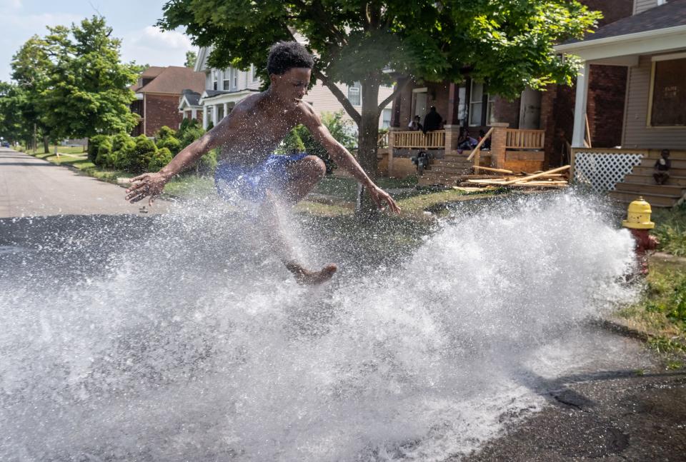 Michael Greer of Detroit jumps over water flowing from an open hydrant on Townsend  Street in Detroit's Islandview neighborhood on Tuesday, July 7, 2020 as the family cools off from the heat wave in the running water.