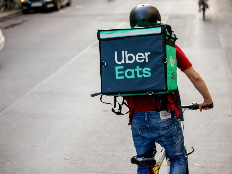 a driver for food delivery service Uber Eats, rides a bicycle with a transport box on his back on a street in the Friedrichshain district of Berlin.