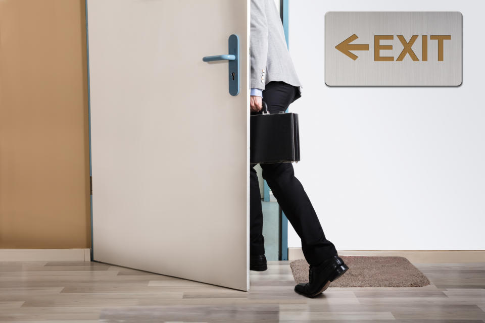 Man with a briefcase walking out a door marked by an exit sign