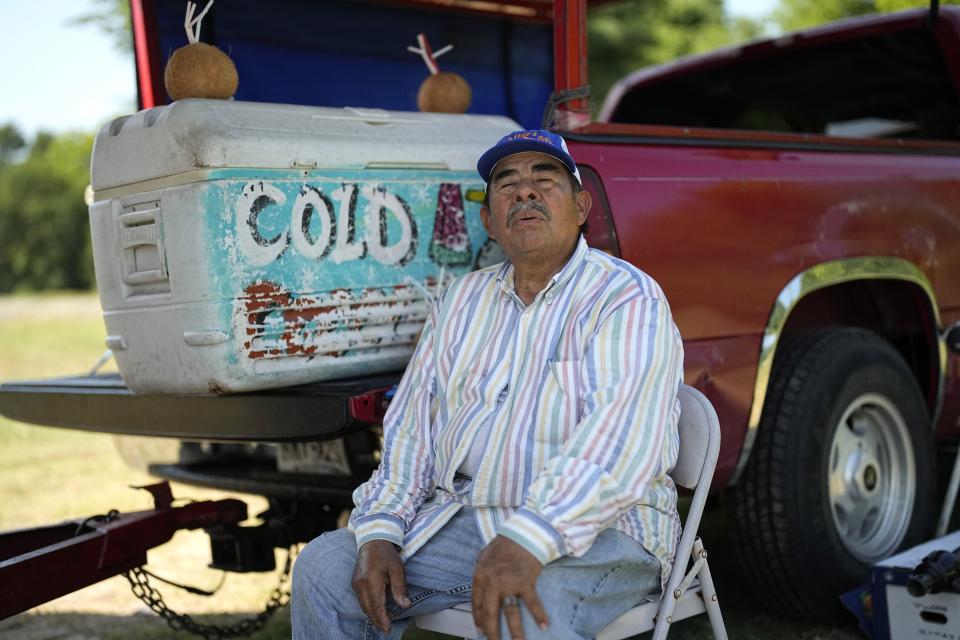 Andres Matamoros sits in the shade as he tries to keep cool while selling fresh fruit and cold coconuts Wednesday, June 28, 2023, in Houston. Meteorologists say scorching temperatures brought on by a heat dome have taxed the Texas power grid and threaten to bring record highs to the state. (AP Photo/David J. Phillip)