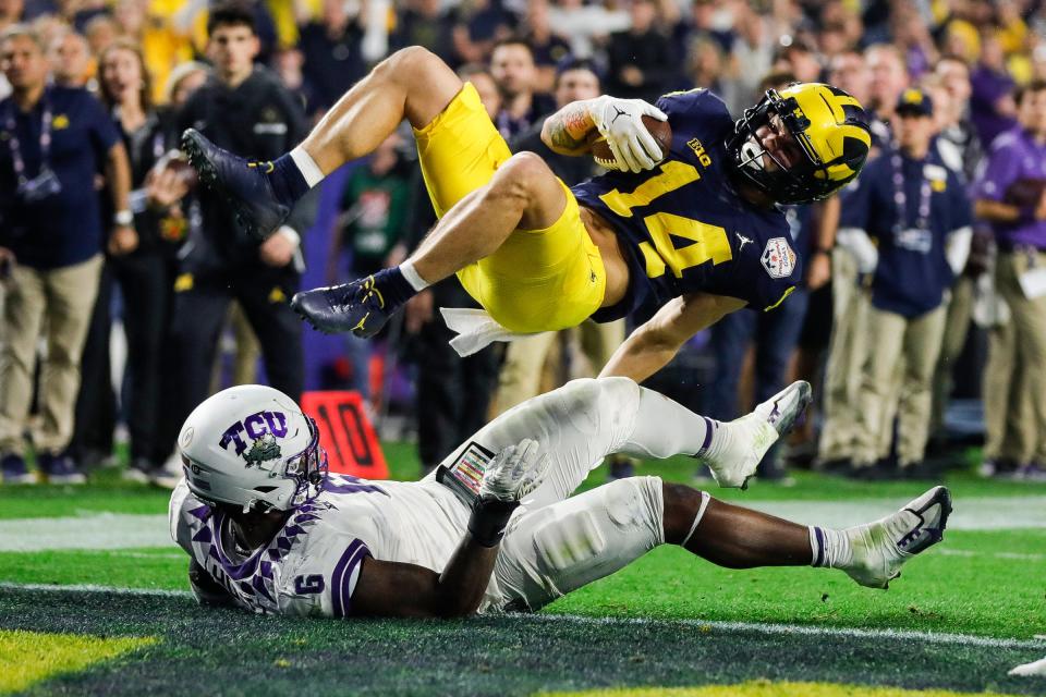 Michigan wide receiver Roman Wilson (14) jumps over TCU linebacker Marcel Brooks (9) for a touchdown during the second half at the Fiesta Bowl at State Farm Stadium in Glendale, Ariz. on Saturday, Dec. 31, 2022.