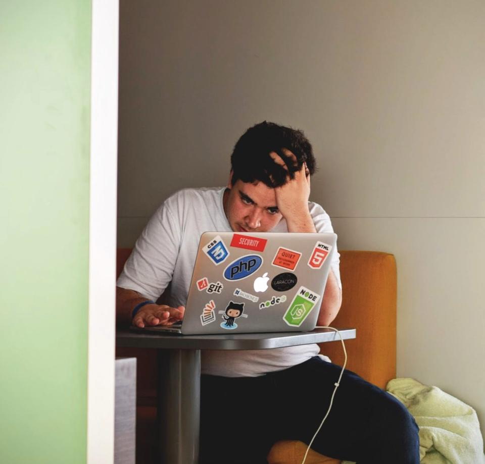 A man runs his hand through his hair and looks agitated while in front of his laptop