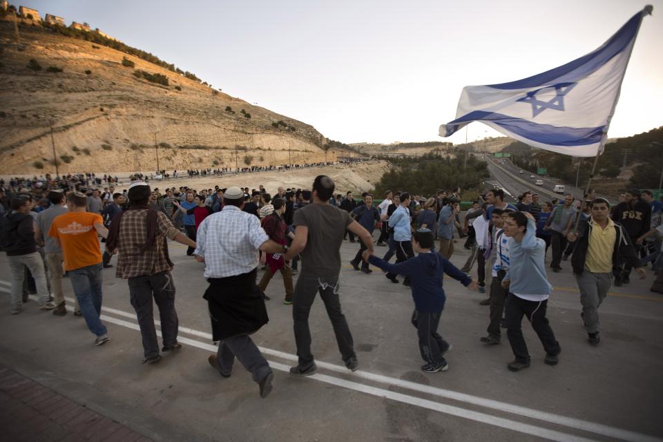 Israelis wave flags and dance as they march from the West Bank settlement of Maaleh Adumim to the E-1 area on the eastern outskirts of Jerusalem, Thursday, Feb. 13, 2014. Israel planned construction in the area E-1, or East 1, but froze under the international pressure in 2009. The construction in the area would effectively separate Palestinians in east Jerusalem from the West Bank. (AP Photo/Sebastian Scheiner)