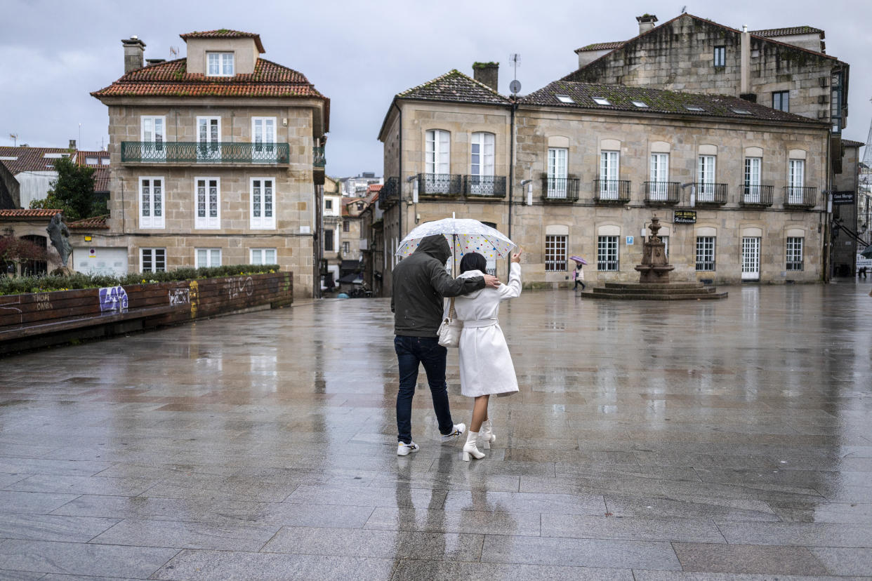 A couple with an umbrella walks across the wet flagstones of a public square in Pontevedra, Spain.