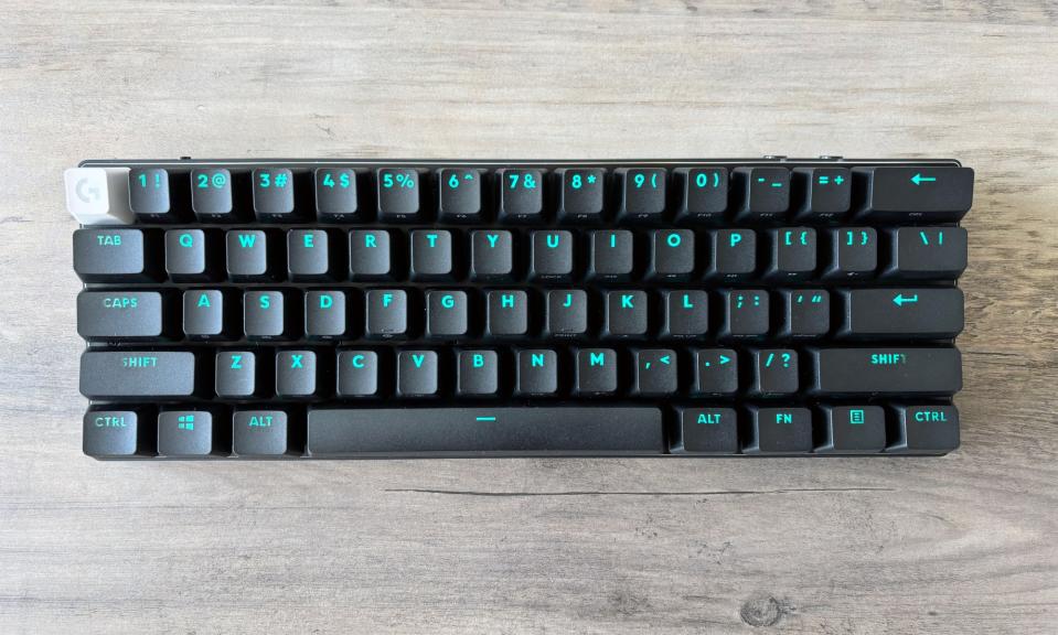 The Logitech G Pro X 60 wireless gaming keyboard in black sits on a wooden tabletop with light blue RGB backlighting displayed through its keycaps.