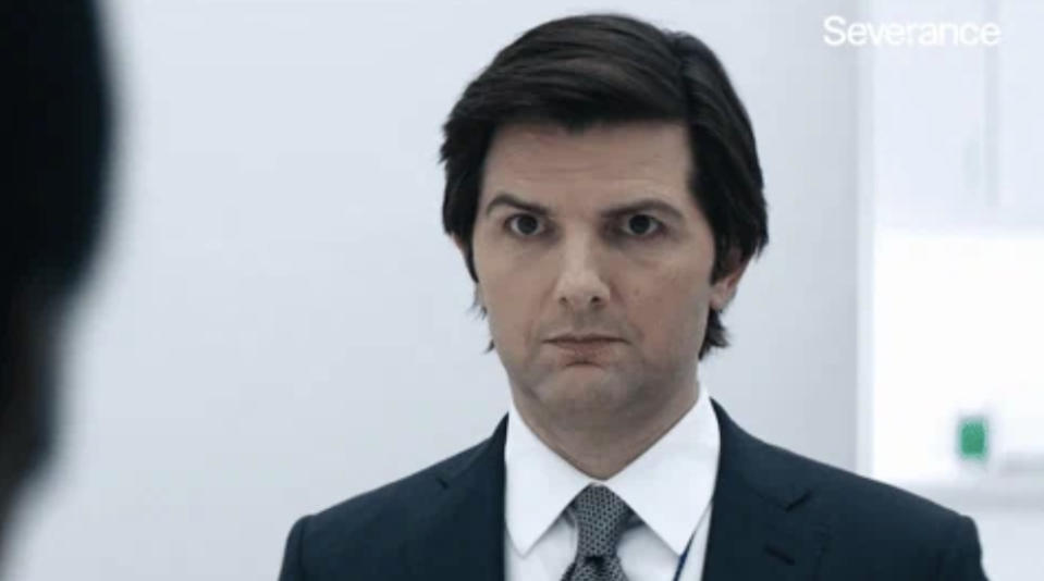 Adam Scott, in a suit and tie, with a serious expression, from the TV show "Severance."