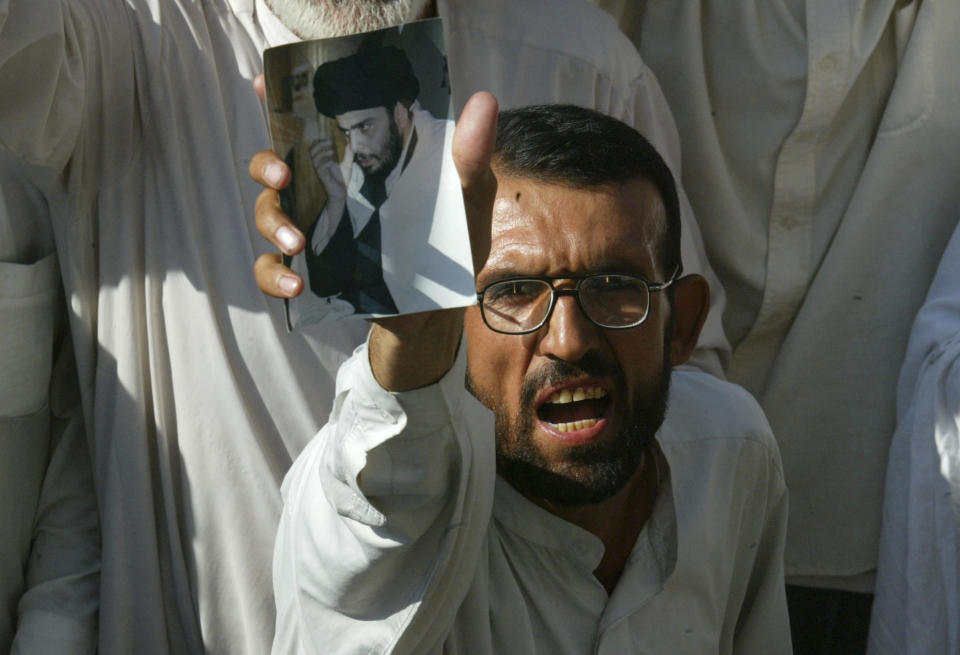 FILE - A Shiite Muslim holds up a photo of Shiite Muslim cleric Muqtada al-Sadr at a protest against U.S. troops Sunday, July 20, 2003, in the Muslim holy city of Najaf, 160 kilometers (100 miles) south of Baghdad, Iraq. Al-Sadr is a populist cleric, who emerged as a symbol of resistance against the U.S. occupation of Iraq after the 2003 invasion. (AP Photo/Mikhail Metzel, File)