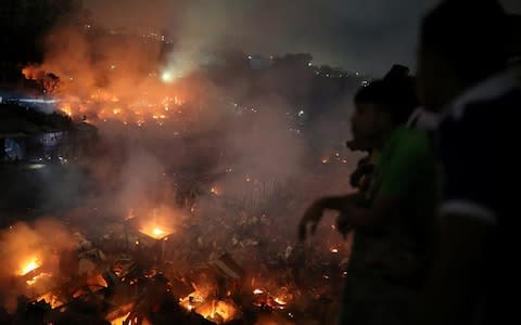 People gather at a rooftop to watch the fire that broke out at a slum in Dhaka, - Credit: REUTERS/Mohammad Ponir Hossain