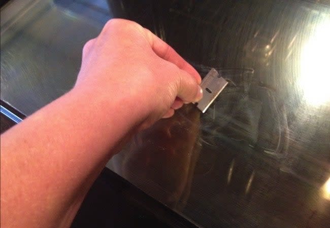 Using a razor blade to scrape debris off oven glass doors.