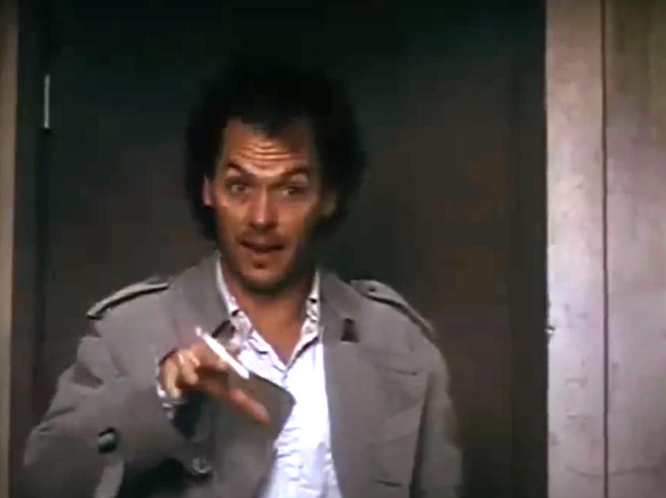 Michael Keaton in a trench coat, holding a cigarette, appears surprised in a scene