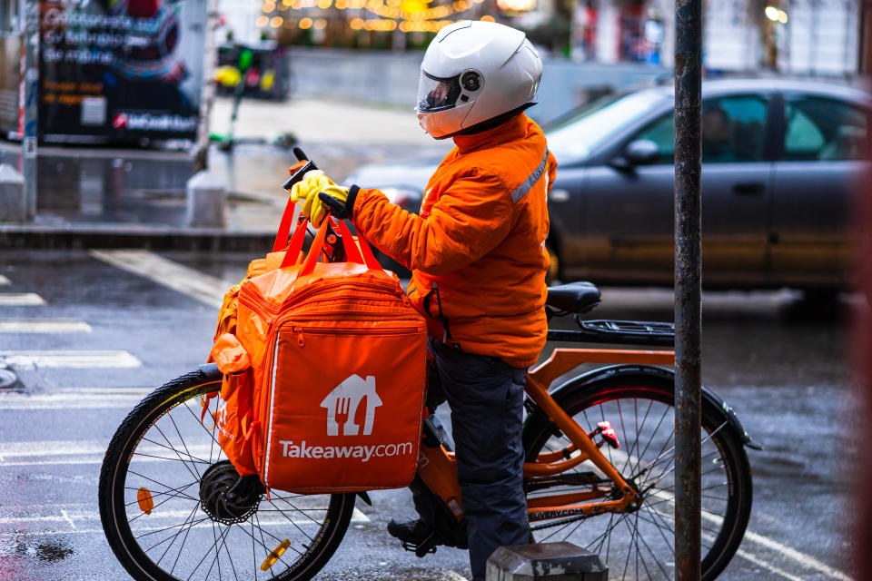 Young man on an electric bike with takeaway.com logo delivering food during a rainy day in Bucharest, Romania, 2020