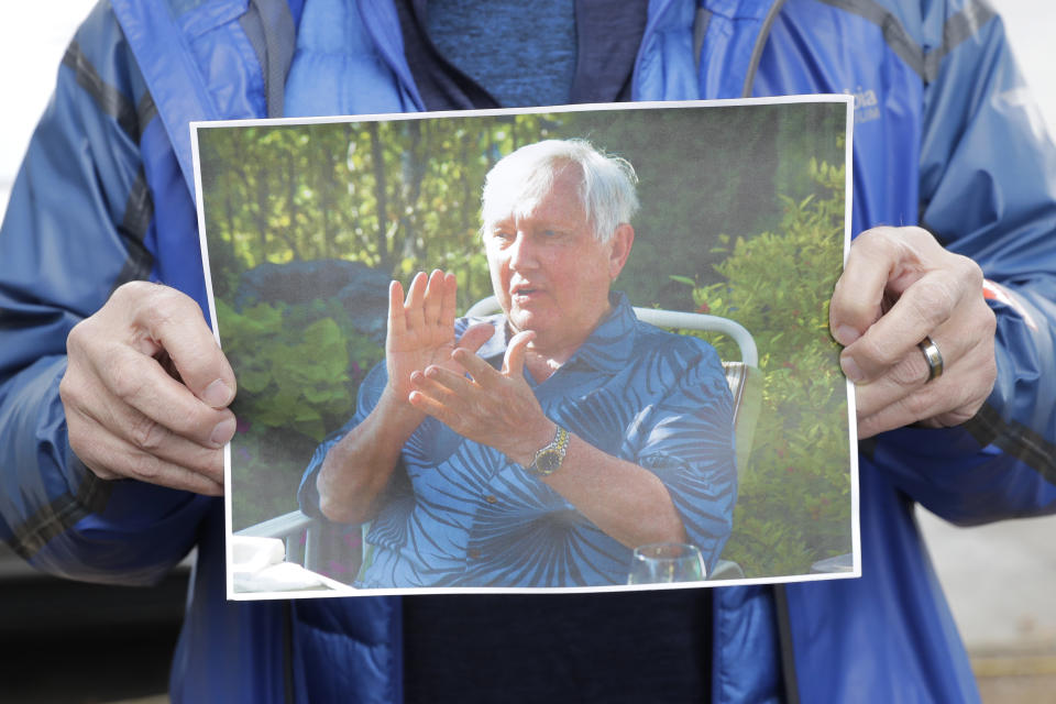 In this March 12, 2020, photo, Scott Sedlacek poses for a photo while holding a picture of his father, Chuck, outside Life Care Center in Kirkland, Wash., near Seattle. The facility has been at the center of the COVID-19 coronavirus outbreak in the state, and Sedlacek — who also has tested positive for the virus — said he and his siblings have barely spoken to their father, who in addition to testing positive for the coronavirus, has blindness, neuropathy, and has difficulty using a phone, saying he is more of an "inmate" than a patient. Residents of assisted living facilities and their loved ones are facing a grim situation as the coronavirus spreads across the country, placing elderly people especially at risk. (AP Photo/Ted S. Warren)