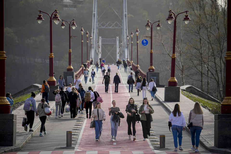 People cross a bridge on a warm afternoon on the bank of the Dniepr River in Kyiv, Ukraine, Tuesday, April 2, 2024. (AP Photo/Vadim Ghirda)