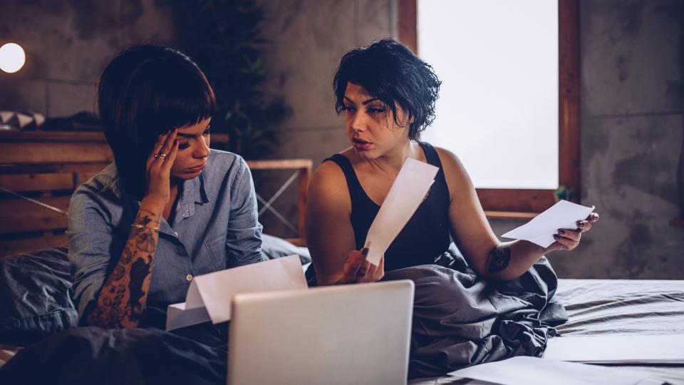 Two girls, young lesbian couple relaxing together at home in bed, looking sad, paying bills.