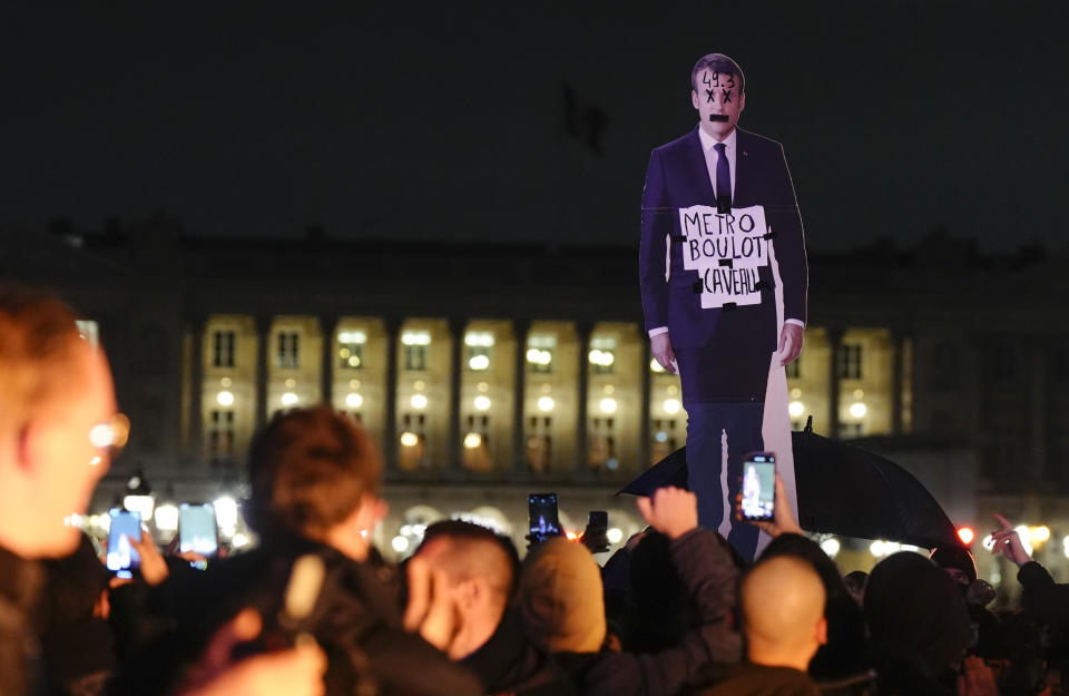 Demonstrators hold a placard depicting French President Emmanuel Macron that reads, "metro, work, grave" during a protest in Paris, Friday, March 17, 2023. Protests against French President Emmanuel Macron's decision to force a bill raising the retirement age from 62 to 64 through parliament without a vote disrupted traffic, garbage collection and university campuses in Paris as opponents of the change maintained their resolve to get the government to back down. (AP Photo/Lewis Joly)