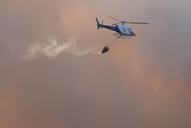 A firefighting helicopter flies amid clouds of smoke from a wildfire burning near houses in Alcabideche, outside Lisbon in July 2023