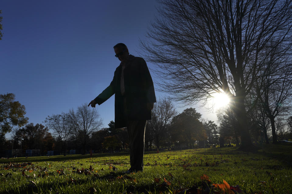 Cook County, Ill., Sheriff's Commander Jason Moran, who leads the sheriff's missing persons initiative stands in silhouette and points to a round cylinder that marks a grave of a person who self-identified as Seven, at the Mount Olivet Cemetery on Chicago's Far South Side Monday, Nov. 13, 2023. “That’s a horrible circumstance that someone could die and no one knows who they are. That’s why we pursue these cases so strongly, out of dignity,” says Moran, who oversees the sheriff’s missing persons unit. “A person deserves a name.” (AP Photo/Charles Rex Arbogast)