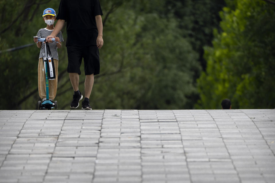 A boy wearing a face mask rides a scooter at a public park in Beijing, Tuesday, June 28, 2022. (AP Photo/Mark Schiefelbein)