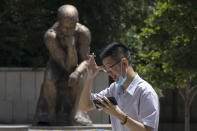 A man lowers his mask to smoke as he passes by a statue in the likeness of The Thinker in Beijing, China on Monday, July 6, 2020. (AP Photo/Ng Han Guan)